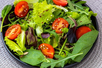Fresh garden salad with assorted greens and cherry tomatoes in a black bowl