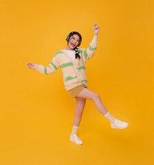 Happy young asian teen woman listening to music with headphone dancing isolated on yellow background. People lifestyle relax concept.