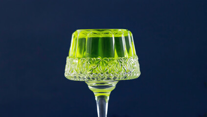 Elegant glass dessert cup filled with vibrant green jelly, showcasing intricate patterns and textures, set against a dark background for a striking visual contrast
