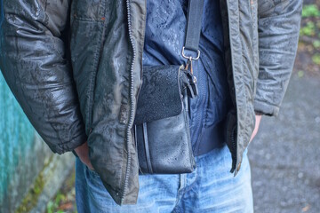 hand of a man in a gray jacket tucked into the pocket of a blue jeans on an autumn street