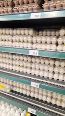 A grocery store shelf filled with various egg cartons. The display includes white and brown eggs,...