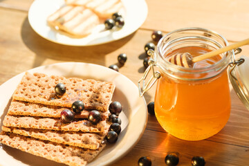 Fresh honey in a jar with a dipper rests next to crunchy crackers and berries on a rustic wooden table, illuminated by warm sunlight, creating an inviting atmosphere.