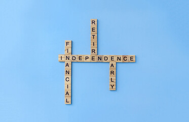 Crossword Financial Independence Retire Early from wooden blocks with letters on blue background. Business FIRE concept. Selective focus and copy space