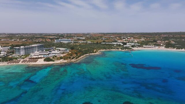 Aerial view of Ayia Napa, Cyprus, showcasing a crescent shaped beach, turquoise waters, lush greenery, and resort buildings with smooth drone motion.
