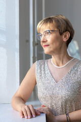 Portrait of smiling woman in festive clothes against a gray wall in a bright sunny room. Vertical photo. High quality photo