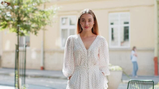 Portrait of happy woman stands with her back and turns around smiling friendly, glad expression looking at camera dreaming, resting, relaxation feel satisfied good news outdoors. Girl on city street.