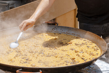 Chef Stirs Mushroom Paella in Wide Pan at Street Food Festival