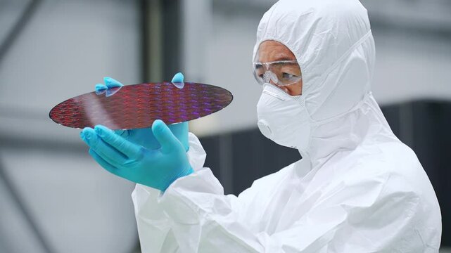半導体工場でシリコンウエハーを検査する防塵服を着た男性作業員