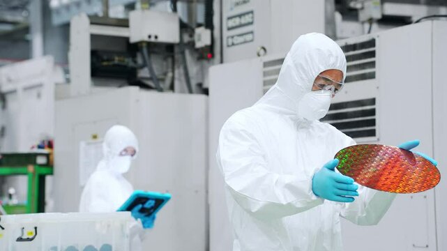 半導体工場でシリコンウエハーを検査する防塵服を着た男性作業員
