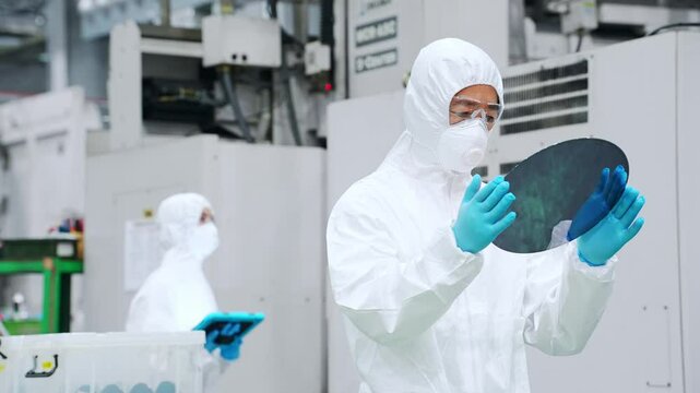 半導体工場でシリコンウエハーを検査する防塵服を着た男性作業員