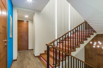 The floor of a private house with brown doors, a staircase with wooden steps and stylish lamps.