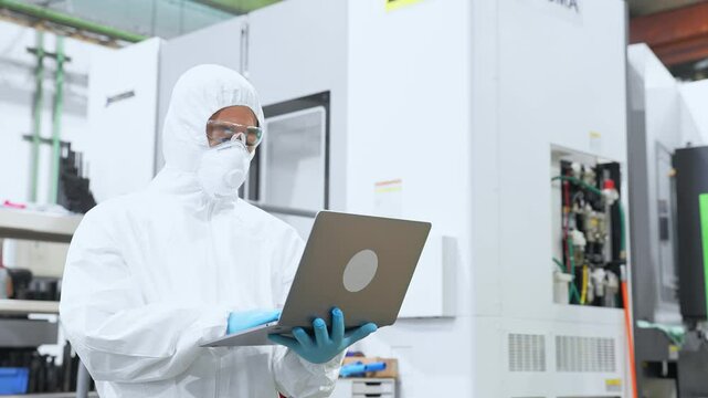 ノートパソコンを持って工場で作業する防護服を着た男性作業員
