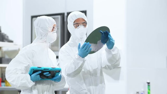 半導体工場でタブレットを持ってシリコンウエハーを検査する防護服を着た男女作業員