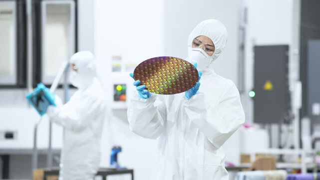 半導体工場でシリコンウエハーを検査する防護服を着た女性作業員
