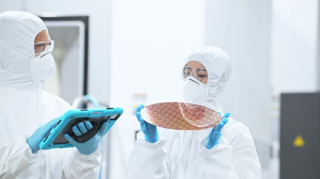 半導体工場でタブレットを持ってシリコンウエハーを検査する防護服を着た男女作業員