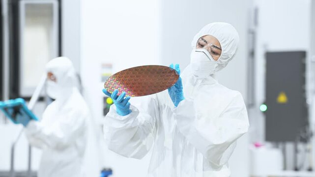 半導体工場でシリコンウエハーを検査する防護服を着た女性作業員