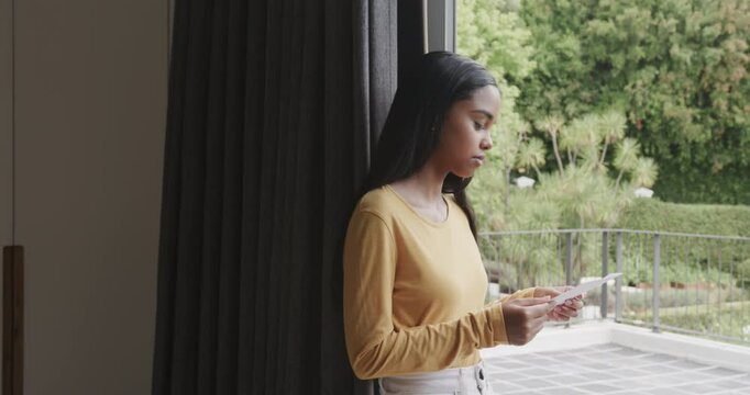 Woman tearing open envelope by sliding glass door reading letter smiling at garden, copy space