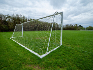 A soccer field with a white goal and a net. The field is green and well-maintained, sport area in a park. Training ground. Cloudy sky. Popular sport.