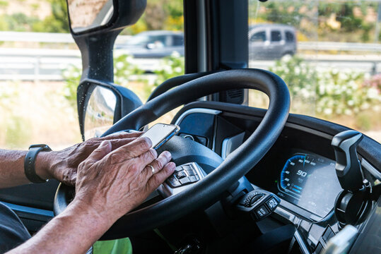 Senior truck driver&rsquo;s hands texting on a mobile phone while driving,illegal, dangerous, and punishable.