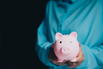 Businessman Holding Pink Piggy Bank Against Dark Background for Saving Money and Financial Planning Concept