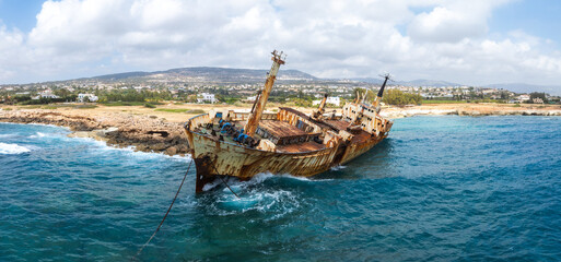 The Edro III Shipwreck leans near Cyprus' rocky coast, with a corroded hull, broken masts, blue...