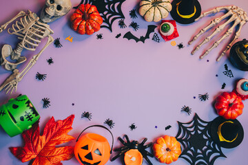 Halloween flat lay. Colorful Halloween Decorations with Skeleton, Pumpkins, Bats, and Spiders on Purple Background