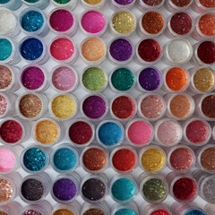 Assorted craft glitters in small containers, isolated art supplies.