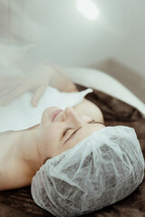 A cosmetologist performs a beauty procedure on the head and face of a young woman.