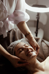A cosmetologist performs a beauty procedure on the head and face of a young woman.
