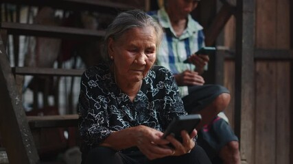 Senior woman using a smartphone sitting on the steps with a man in the background who also uses a phone - Powered by Adobe