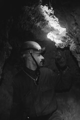a young caving instructor dressed in a protective suit and helmet shows the route in a cramped gypsum cave