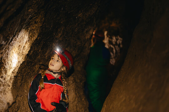 A 6-year-old girl in a protective suit and helmet with a flashlight in the middle of a natural underground cave is walking the tourist route of a caver