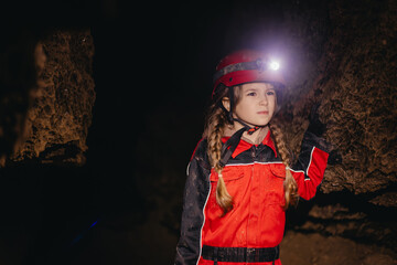 A 6-year-old girl in a protective suit and helmet with a flashlight in the middle of a natural...