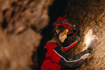 A 6-year-old girl in a protective suit and helmet with a flashlight in the middle of a natural...