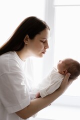 Loving mother carying of her newborn baby at home. Bright portrait of happy mum holding cute infant child on hands. Mother hugging her little 1 months old daughter