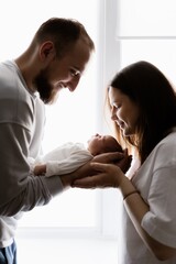 Portrait of a young family with infant in his arms photographed on a light window background.