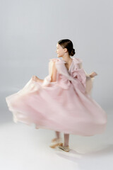 A young girl in a flowing pink dress twirls joyfully against a plain background.