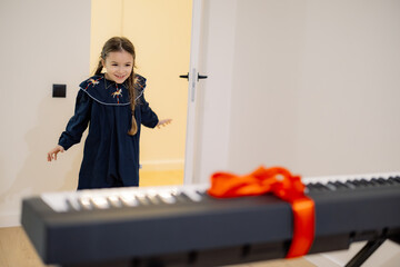 A young girl excitedly opens a gift-wrapped keyboard with a red ribbon.