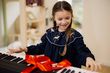 A young girl excitedly opens a gift-wrapped electronic keyboard with a red ribbon.