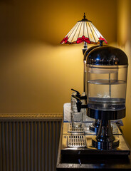 A hotel water cooler station with a beautiful stained-glass lamp in the background. 