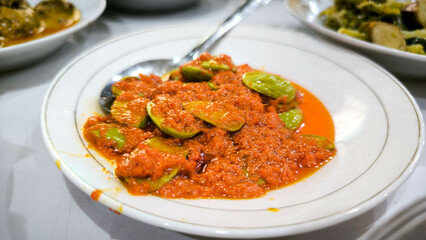 Traditional Indonesian sambal with petai beans served on a white plate, spicy red chili sauce as the main dish on a dining table.