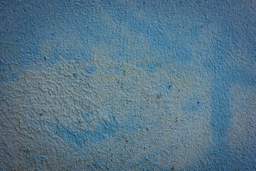 A close-up of a rough, weathered concrete wall with peeling light blue paint, revealing intricate textures and faded hues, suitable for an abstract background.

