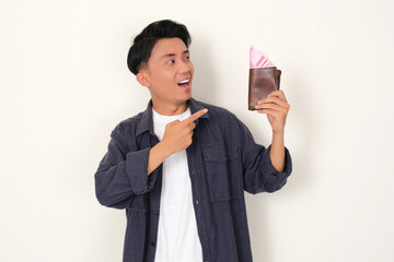 Young Asian man showing happy face while looking and pointing at wallet full of money that he hold