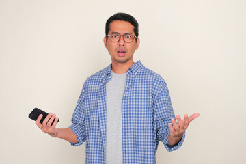Adult Asian man holding mobile phone showing worried face expression