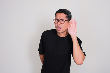 Adult Asian man listening something with hand on his ear showing worried expression