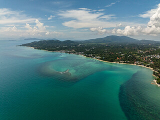 A scenic tropical island with bright turquoise water and lush green hills under a sunny sky. Koh Samui, Thailand.