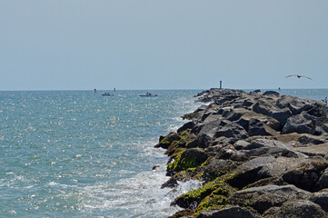 Seascape view of Ponce Inlet jetty rocks leading into the ocean, the horizon dotted with fishing...