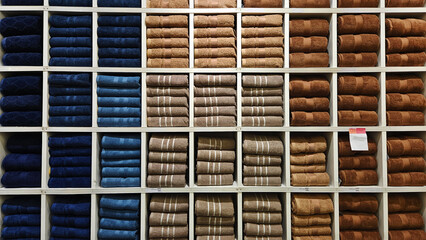 Many groups stack blue, brown, gray, or grey towels on a white wooden shelf for sale with a price tag and copy space at the department store.