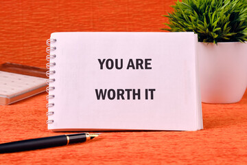 YOU ARE WORTH IT words on a spiral notebook on an orange background