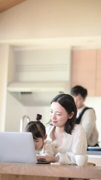 自宅のリビングで仕事をするママと家事をするパパ　リモートワーク、共働きや主夫のイメージ縦動画